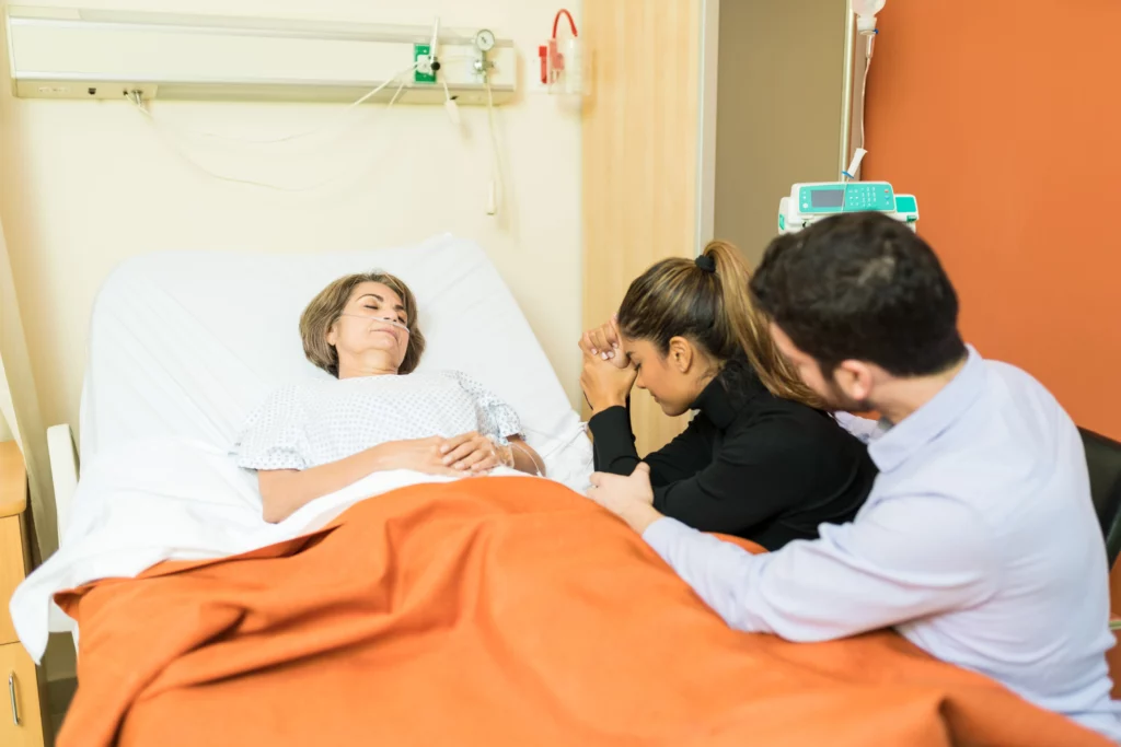 Woman in hospital bed with two visitors holding her hands, symbolizing medical decision support