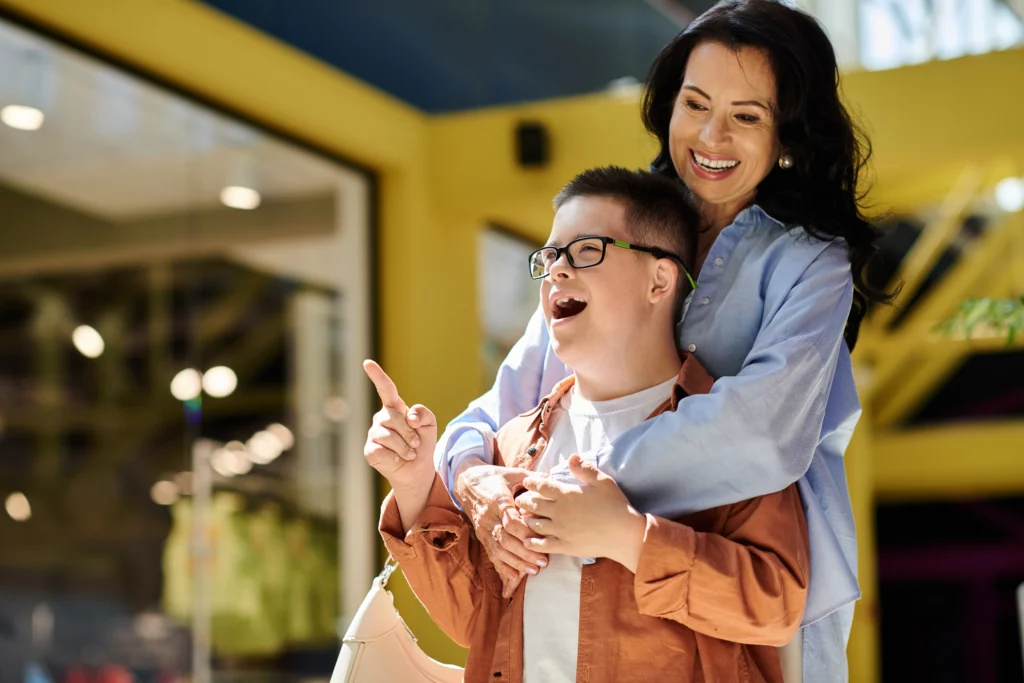 Woman hugging joyful boy with glasses outdoors in front of yellow building — representing Florida special needs support